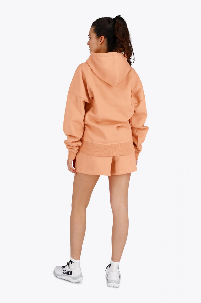 Woman wearing the Osaka women hoodie in peach with white logo. Back view