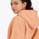 Woman wearing the Osaka women hoodie in peach with white logo. Back detail cap view