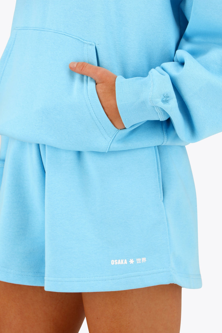 Woman wearing the Osaka women hoodie in light blue with white logo. Front detail sleeve view
