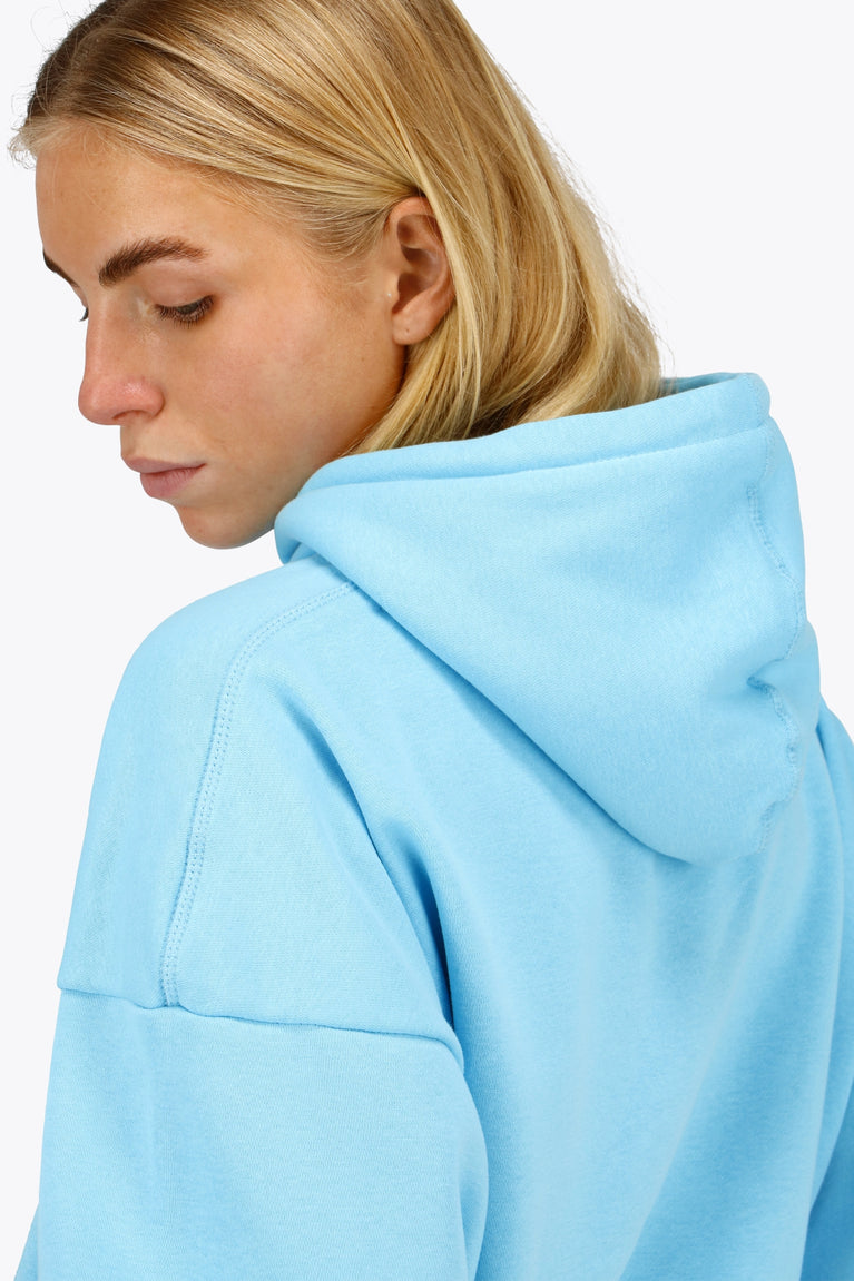 Woman wearing the Osaka women hoodie in light blue with white logo. Side detail cap view