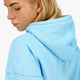Woman wearing the Osaka women hoodie in light blue with white logo. Side detail cap view