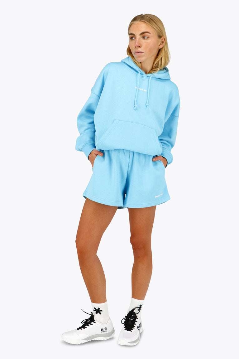 Woman wearing the Osaka women hoodie in light blue with white logo. Front view