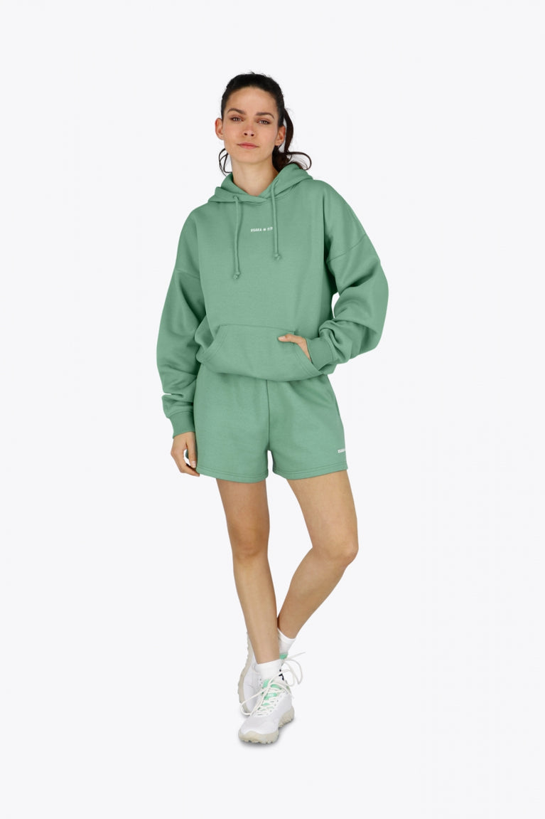 Woman wearing the Osaka women hoodie in green with white logo. Front view