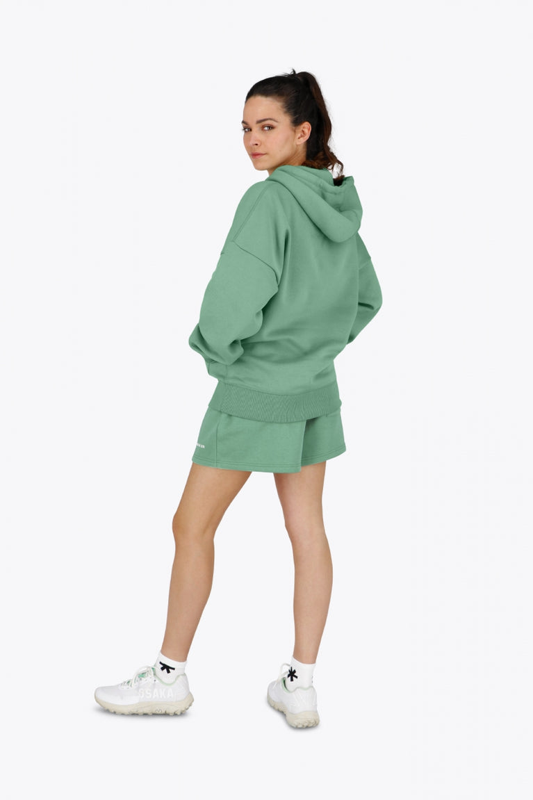 Woman wearing the Osaka women hoodie in green with white logo. Side back view