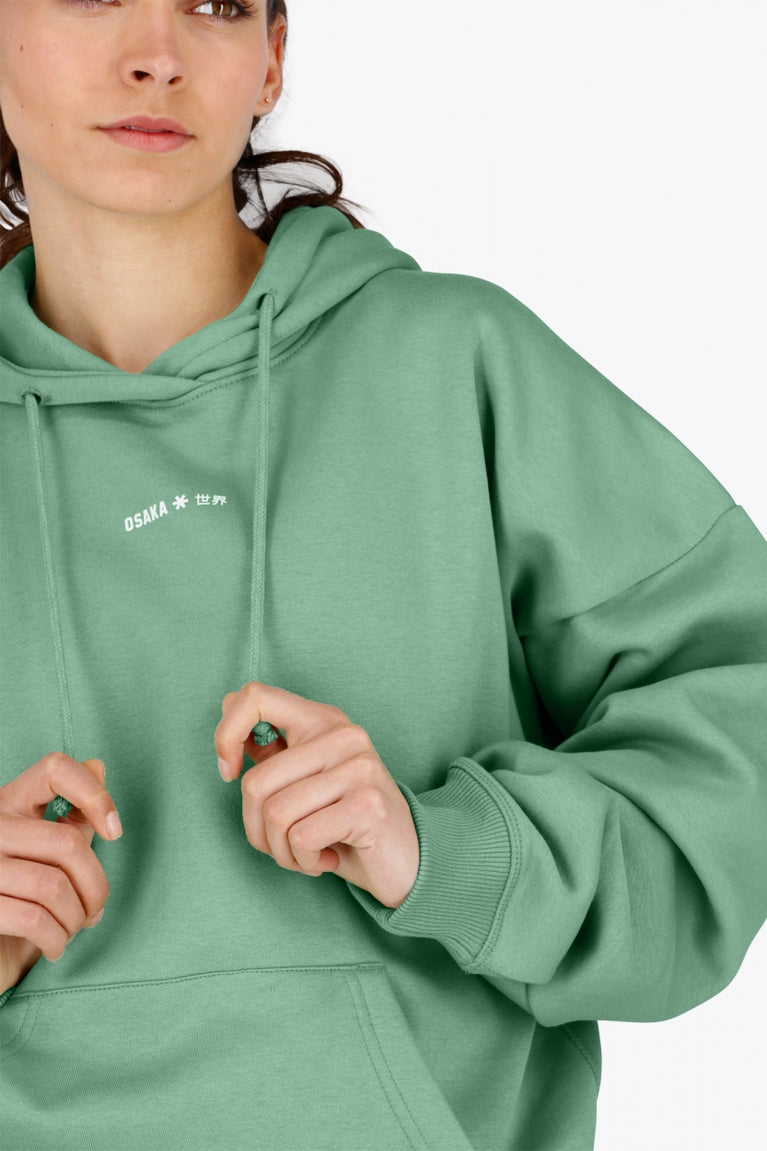 Woman wearing the Osaka women hoodie in green with white logo. Front detail view