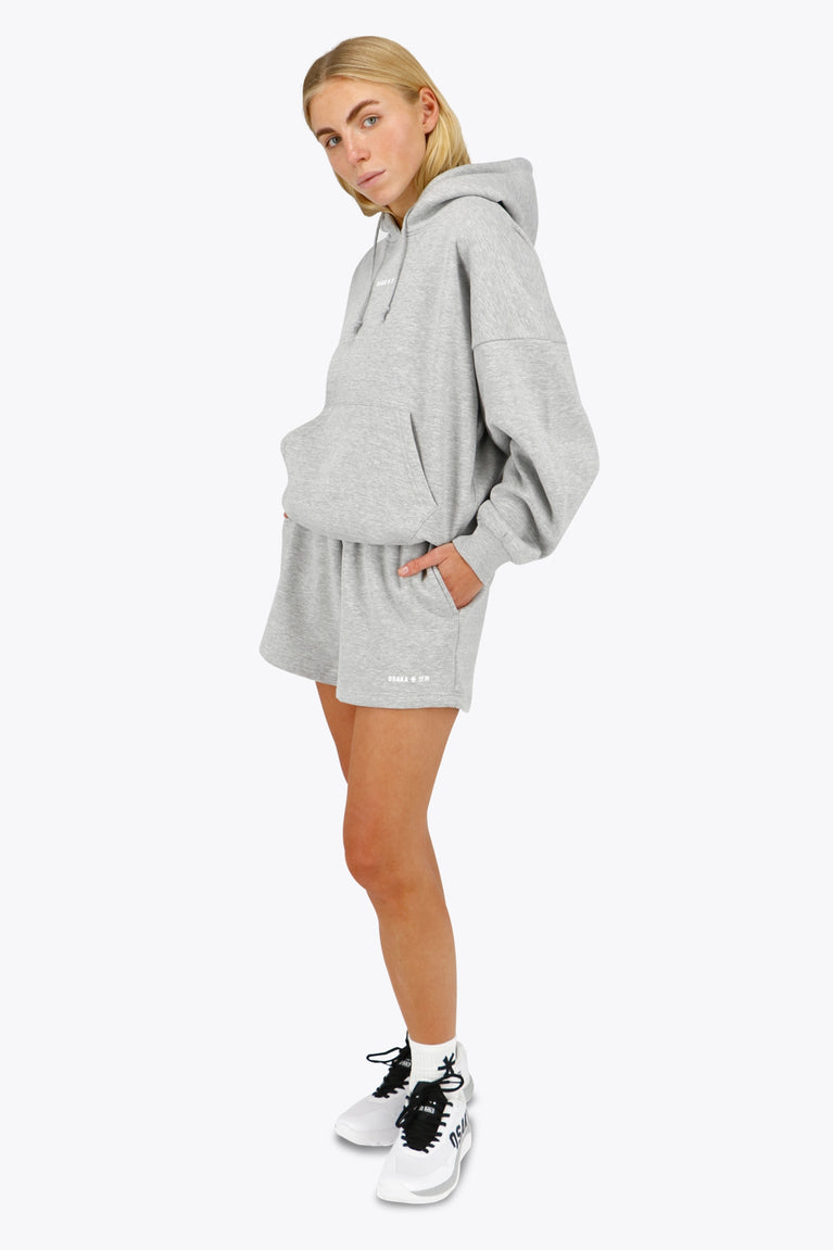 Woman wearing the Osaka women hoodie in heather grey with white logo. Front / side view