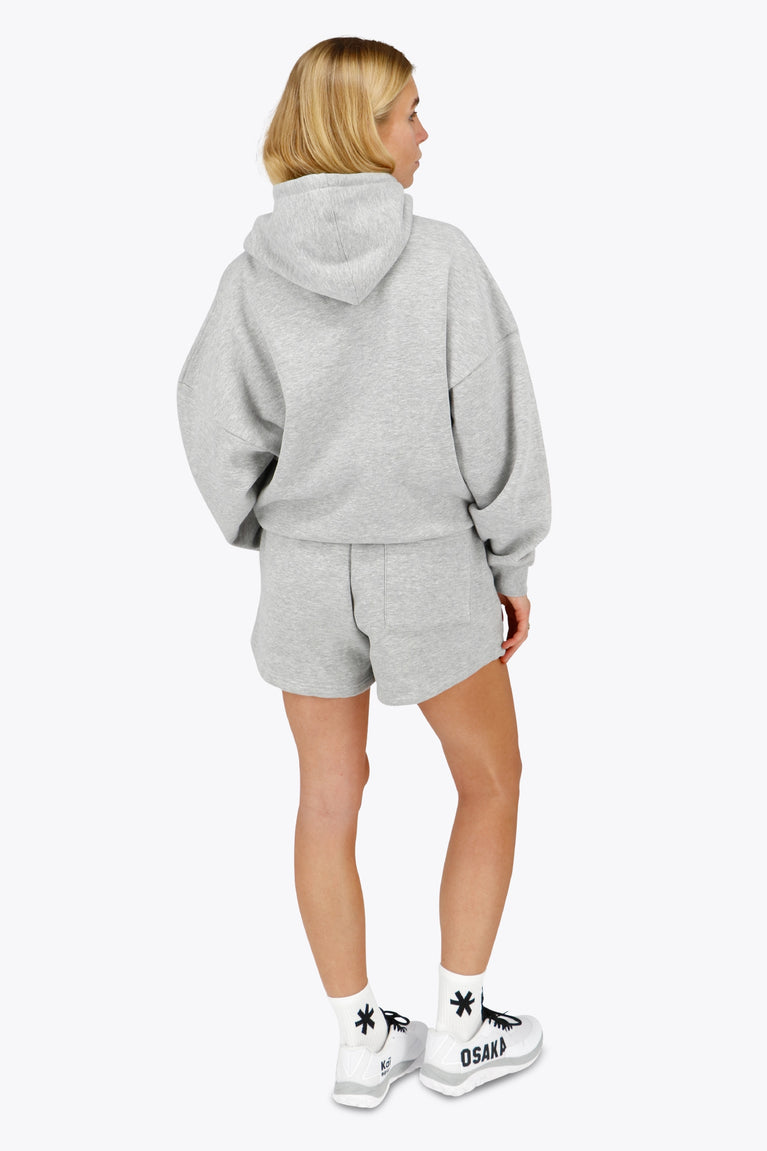 Woman wearing the Osaka women hoodie in heather grey with white logo. Back view