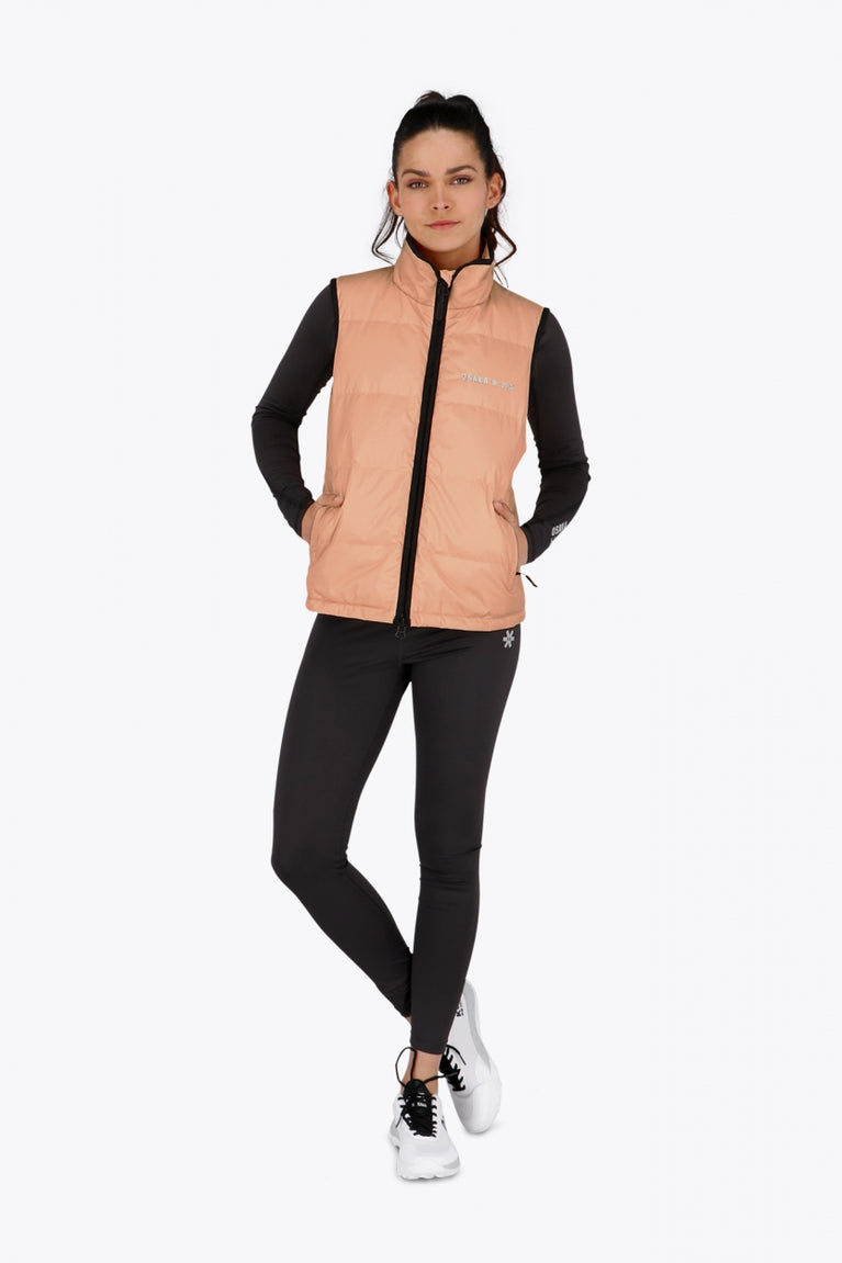 Woman wearing the Osaka women padded gilet in peach with grey logo. Front view