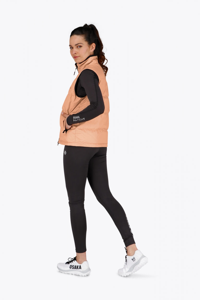 Woman wearing the Osaka women padded gilet in peach with grey logo. Back view