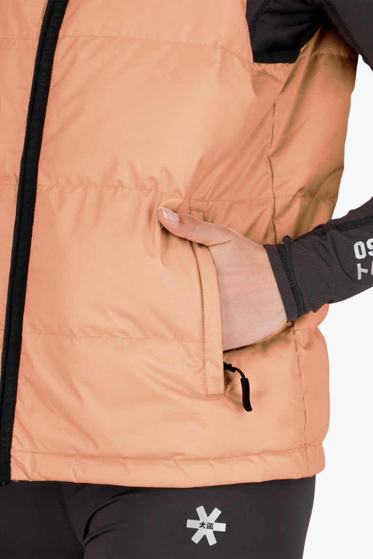 Woman wearing the Osaka women padded gilet in peach with grey logo. Front detail pocket view