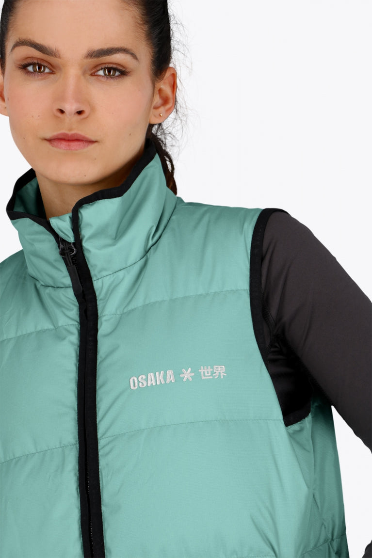 Woman wearing the Osaka women padded gilet in green with grey logo. Front detail logo view