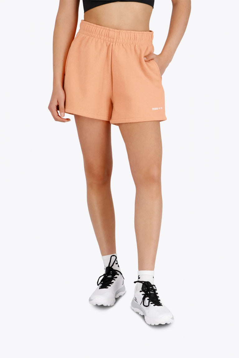 Woman wearing the Osaka women shorts in peach with logo in white. Front view