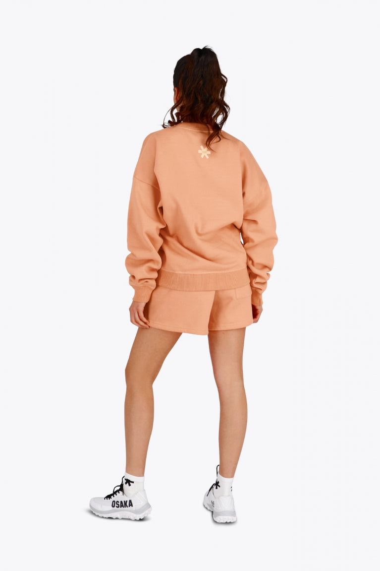 Woman wearing the Osaka women sweater in peach with logo in white. Back view