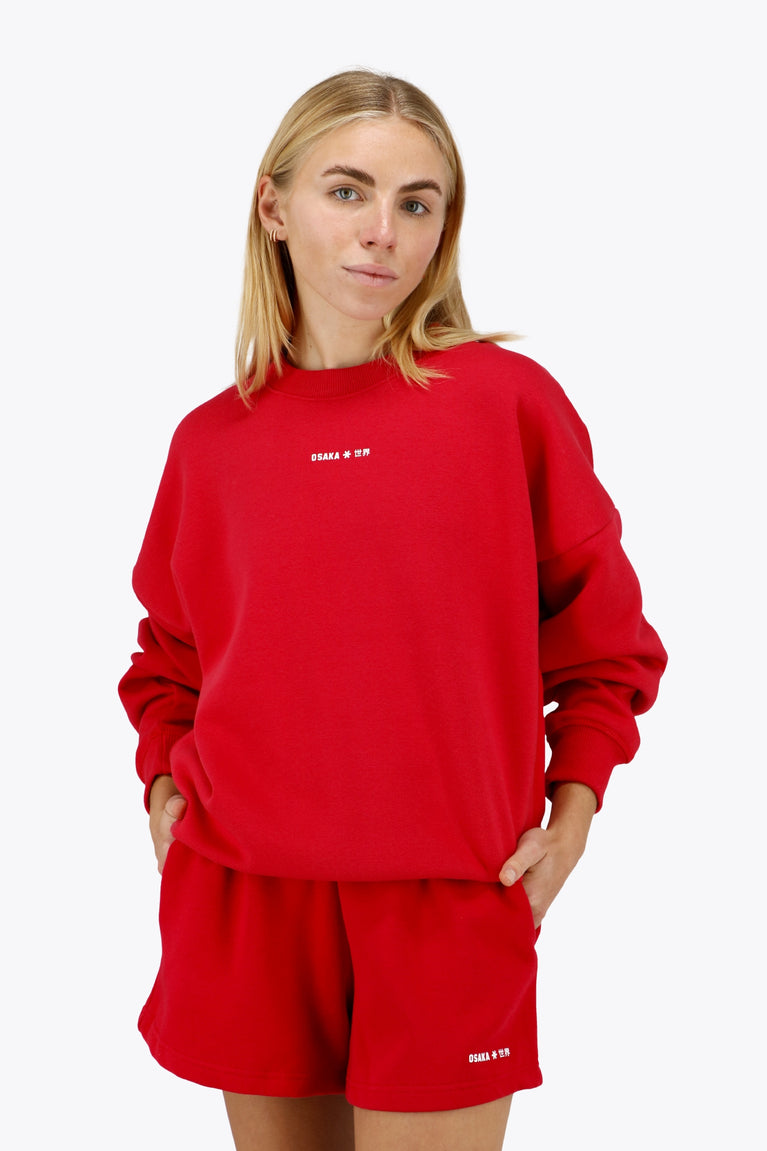 Woman wearing the Osaka women sweater in red with logo in white. Front view