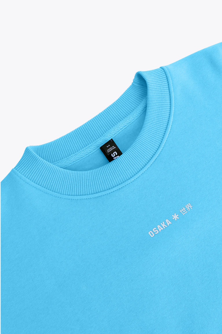 Osaka women sweater in light blue with logo in white. Front flatlay logo view