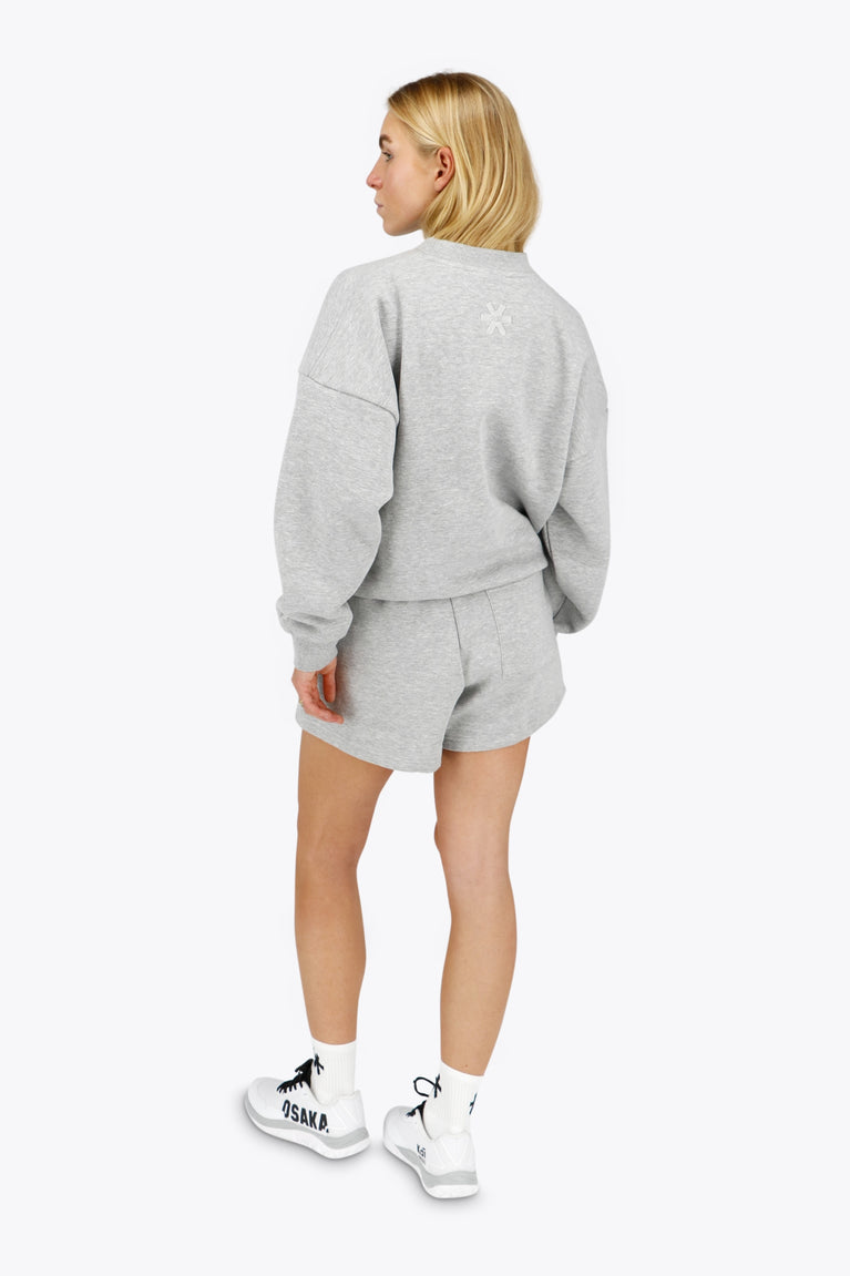 Woman wearing the Osaka women sweater in heather grey with logo in white. Back view