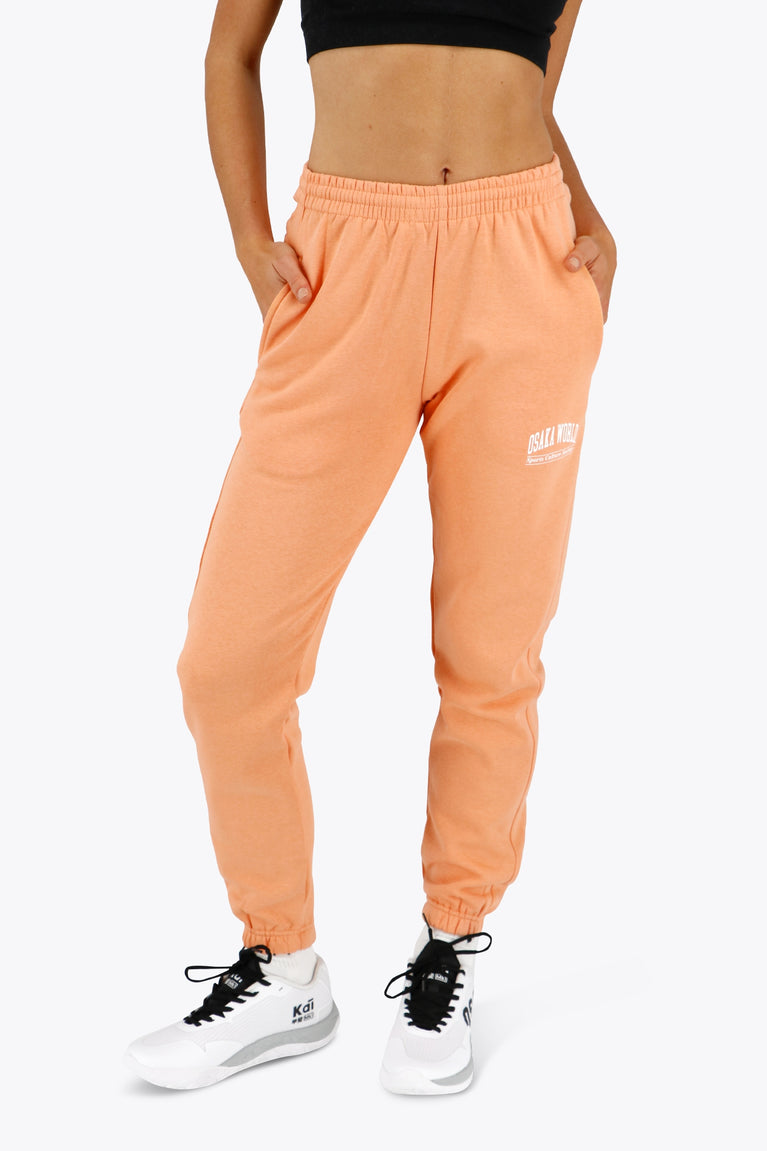 Woman wearing the Osaka women sweatpants in peach with logo in white. Front view