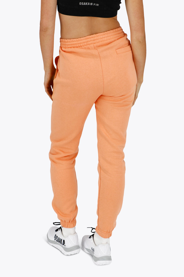 Woman wearing the Osaka women sweatpants in peach with logo in white. Back view
