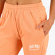 Woman wearing the Osaka women sweatpants in peach with logo in white. Front detail logo view