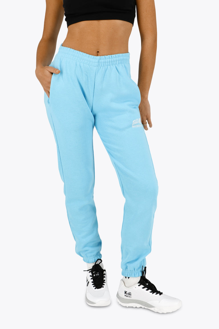 Woman wearing the Osaka women sweatpants in light blue with logo in white. Front view
