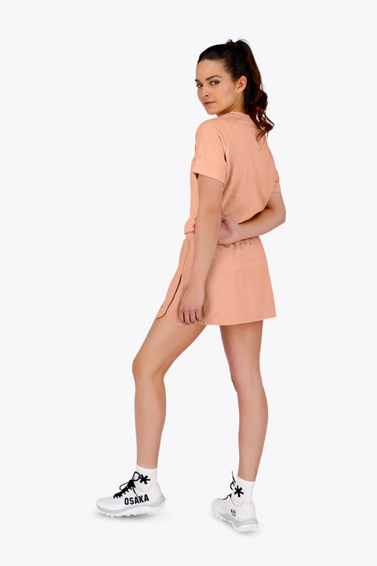Woman wearing the Osaka women tee short sleeve in peach with logo in grey. Back view