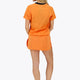 Woman wearing the Osaka women tee short sleeve in orange with logo in grey. Back view