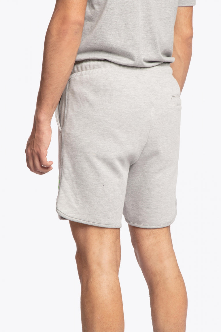 Man wearing the Osaka Men padel shorts in grey with green logo on it. Back / side view