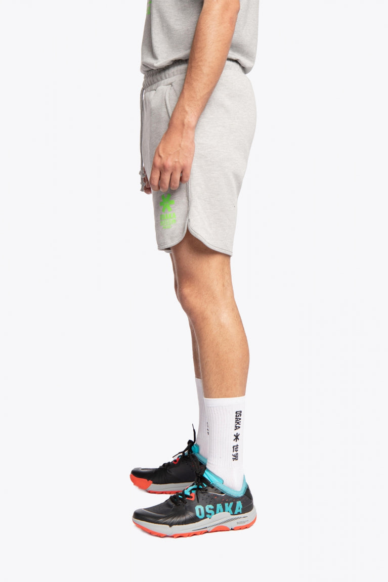 Man wearing the Osaka Men padel shorts in grey with green logo on it. Side view
