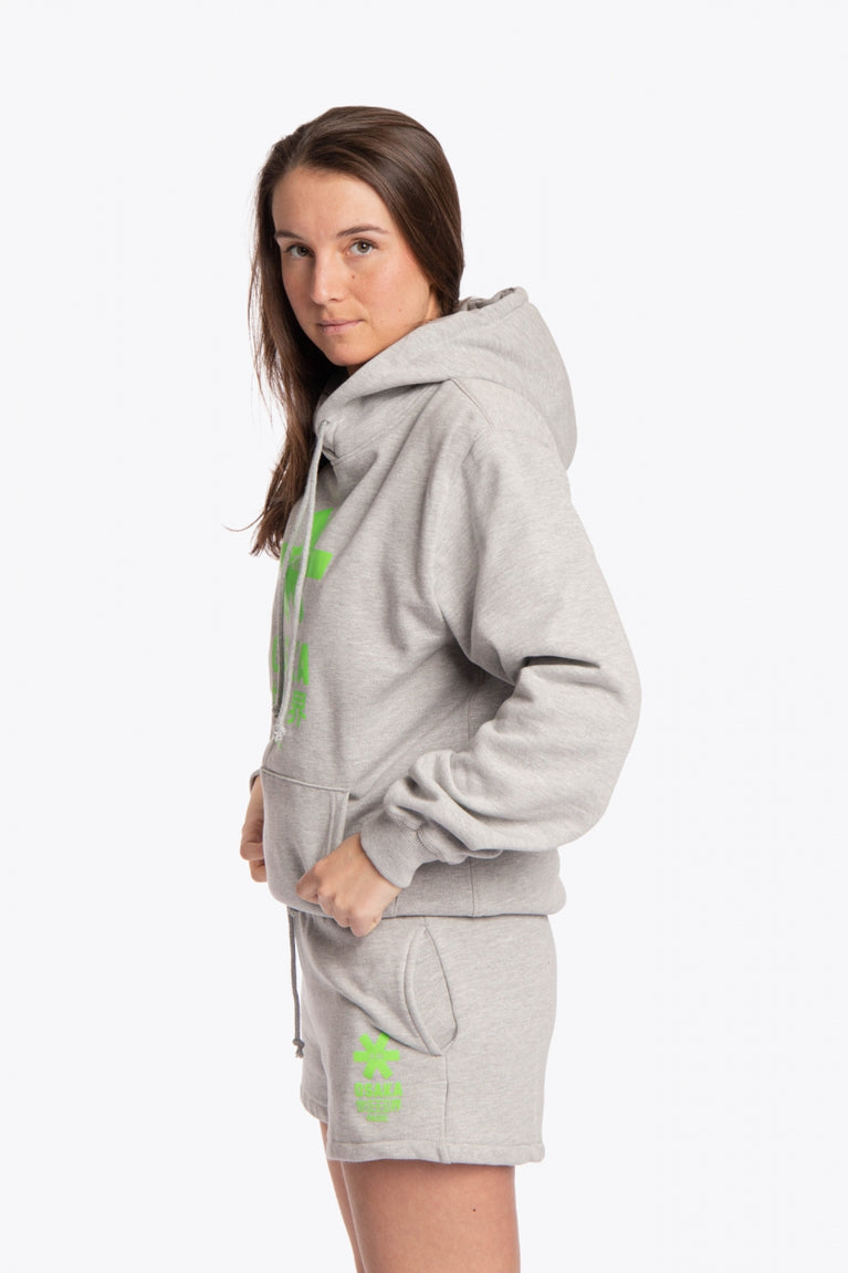 Woman wearing the Osaka basic unisex hoodie in grey with green logo on it. Side view
