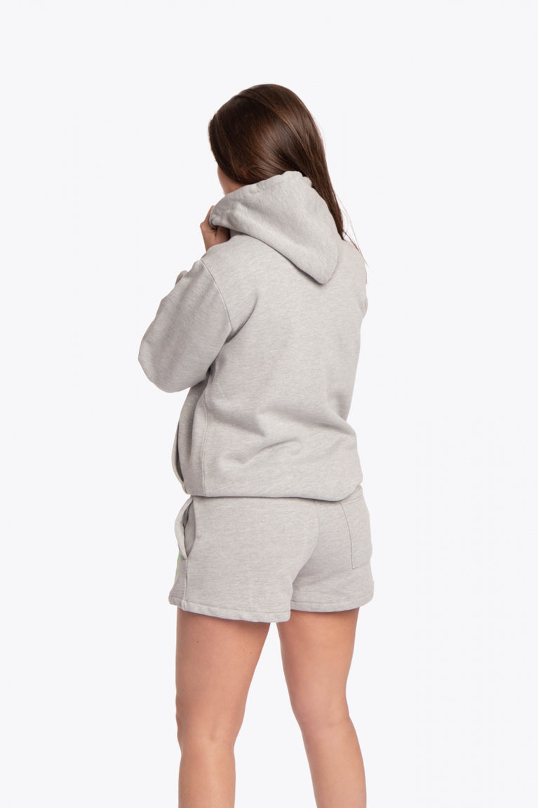 Woman wearing the Osaka basic unisex hoodie in grey with green logo on it. Back view