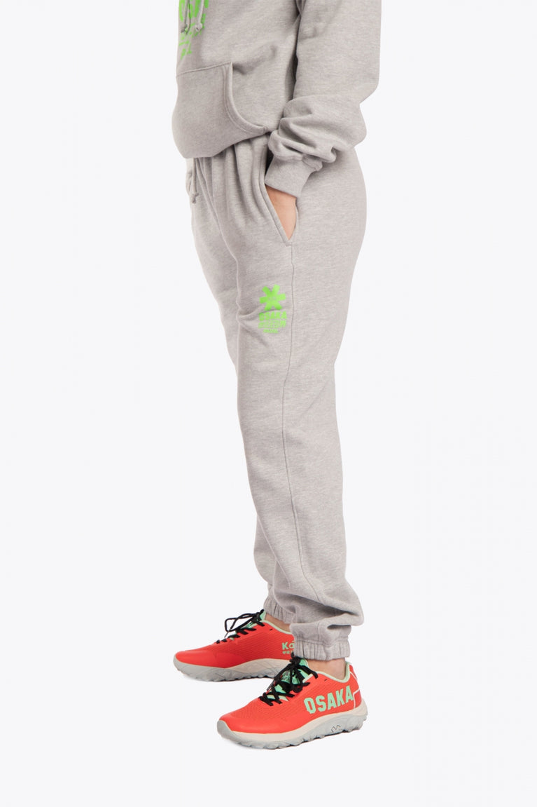 Model wearing the Osaka unisex sweatpants in heather grey with logo in green. Side view