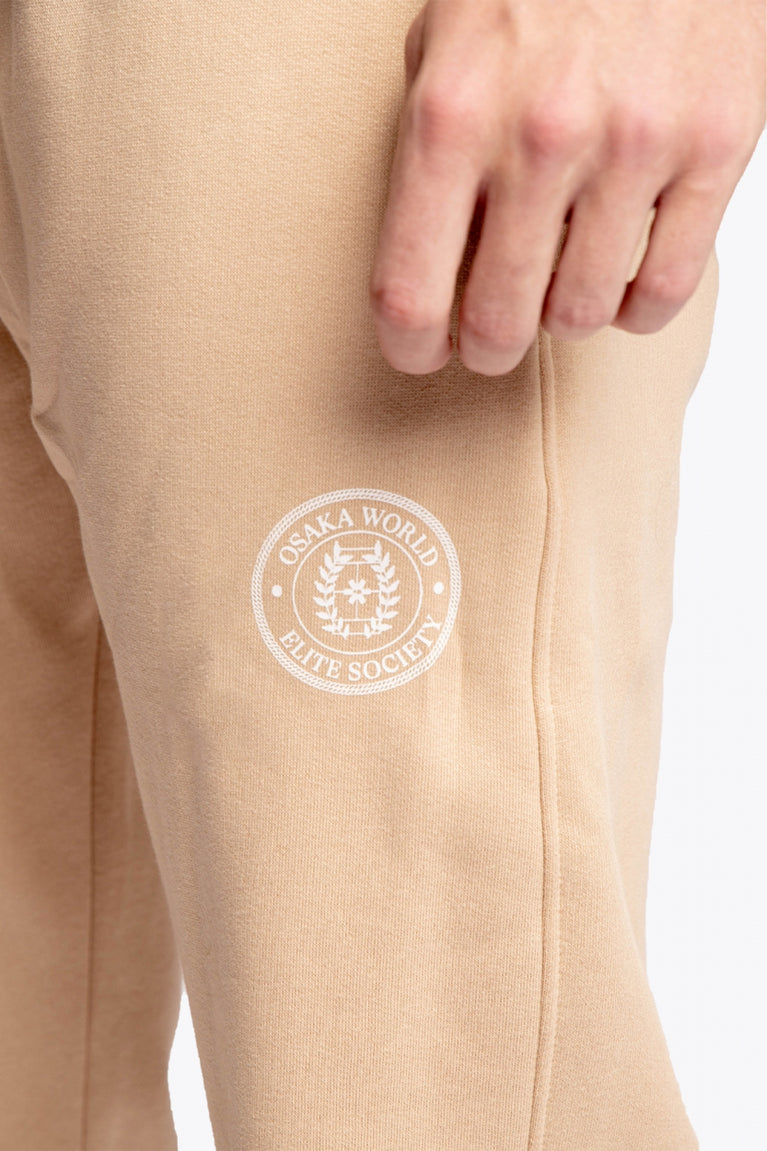 Model wearing the Osaka unisex sweatpants in stone with logo in white. Detail logo view