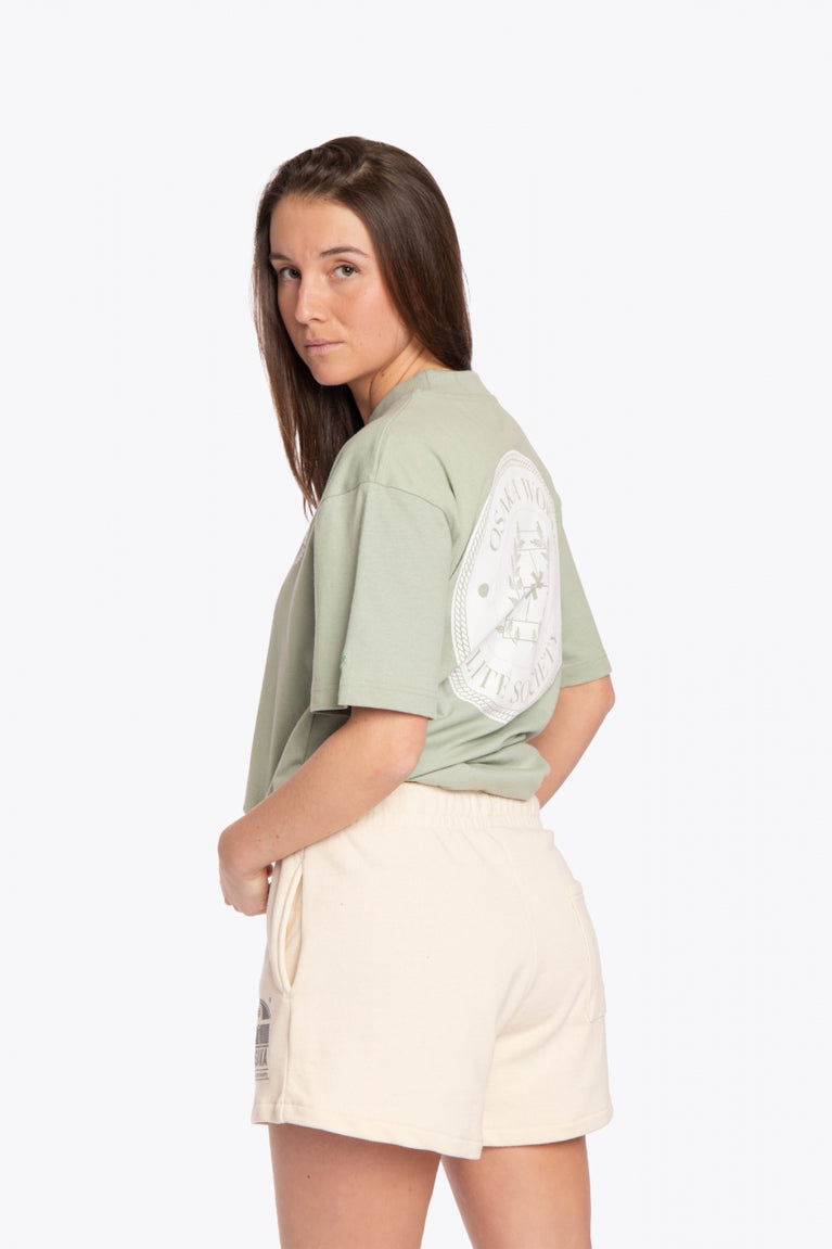 Woman wearing the Osaka unisex tee in iceberg green with white logo. Side back view