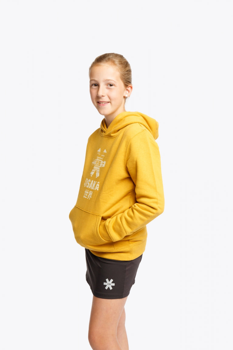Girl wearing the Osaka kids hoodie in ochre and marker logo in white. Front/side view