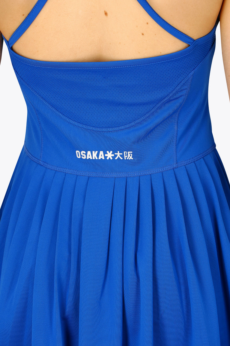 Woman wearing the Osaka women pleated tech dress in princess blue with grey logo. Back detail logo view