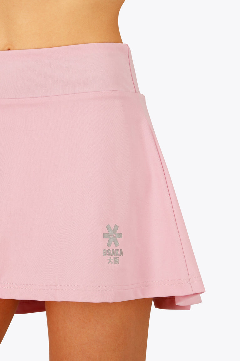 Woman wearing the Osaka women floucy skort pink with logo in grey. Front detail logo view
