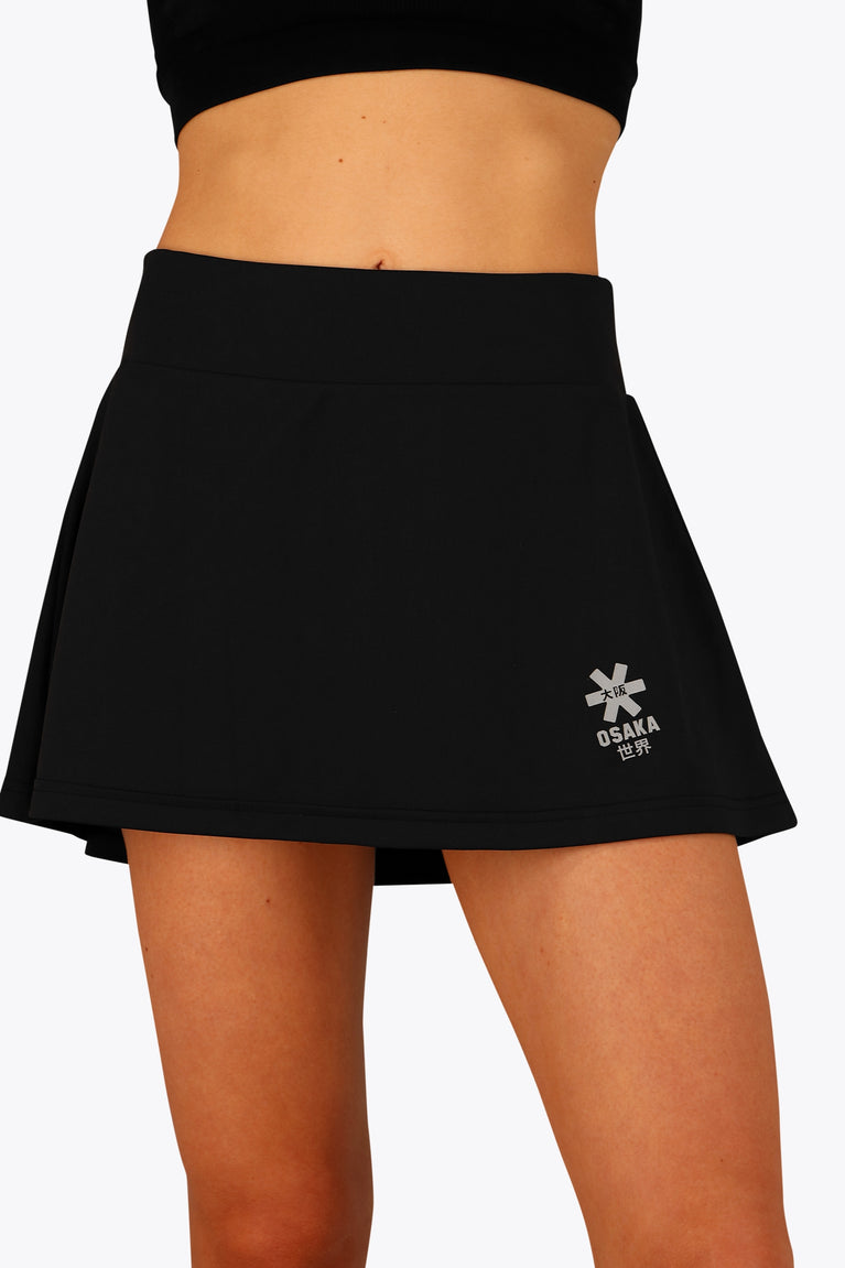 Woman wearing the Osaka women floucy skort black with logo in grey. Front detail view