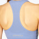 Woman wearing the Osaka women tech sports bra in manor blue with logo in grey. Back view