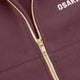 Plum zip-up sweater close-up showing gold zipper and embroidered chest logo