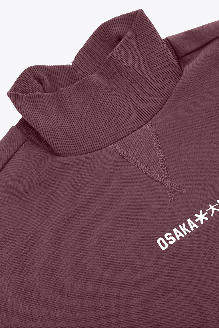 Women’s mockneck sweater close-up: ribbed collar and Osaka* chest logo on dark plum