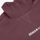Women’s mockneck sweater close-up: ribbed collar and Osaka* chest logo on dark plum