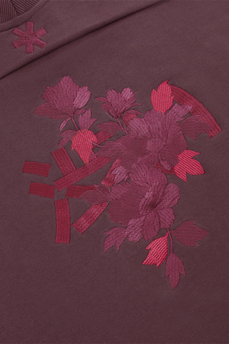 Women’s mockneck sweater close-up of red floral applique on dark plum fabric