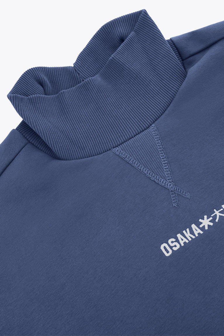 Blue mockneck sweater detail with ribbed collar and Osaka* logo embroidery