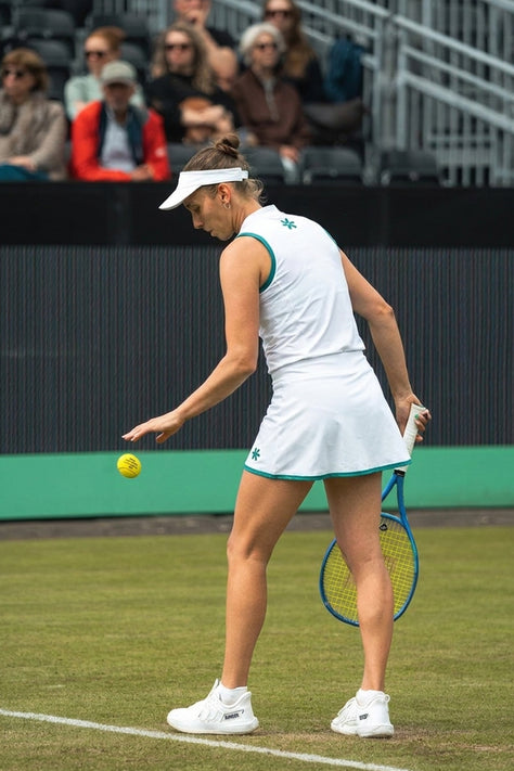 White women’s court tank top with green logo on chest and green-trim armholes.