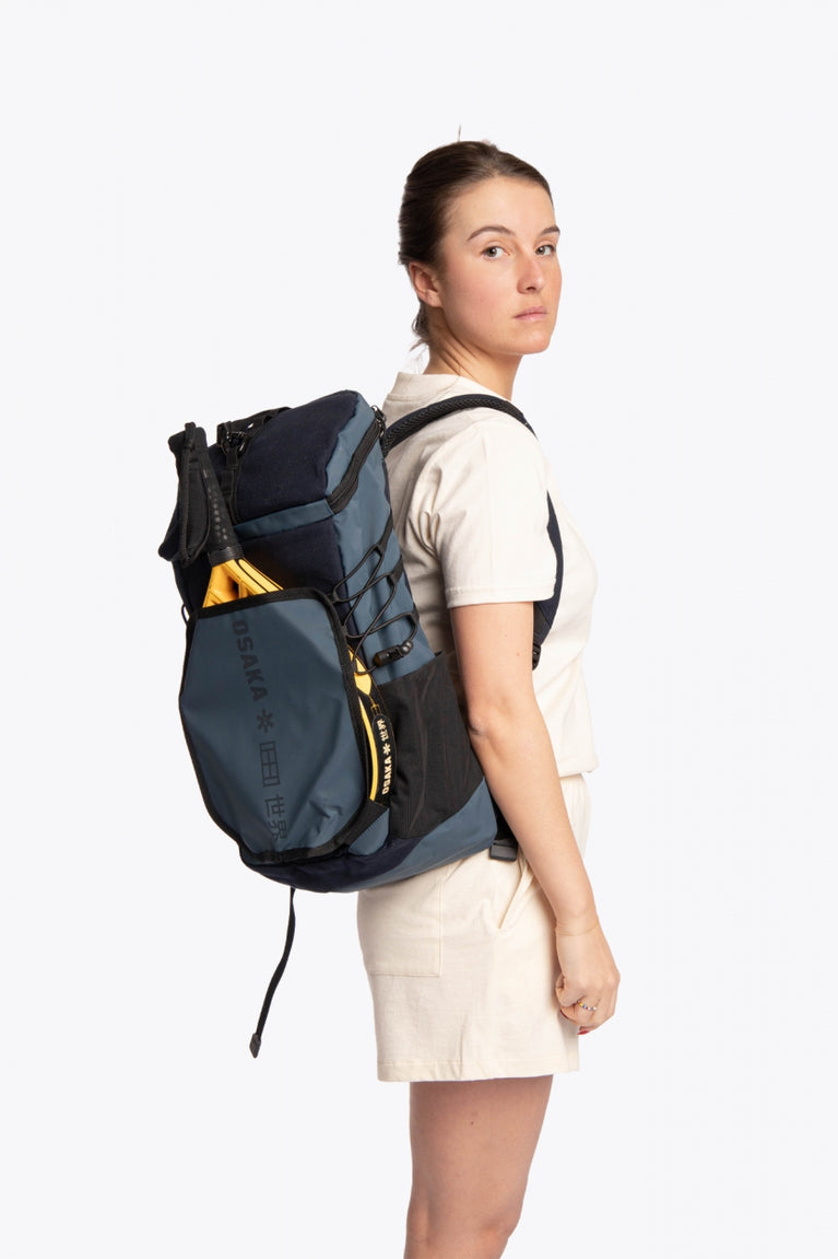  Pro Tour padel backpack in navy with logo in black. Woman wearing the bag, side view