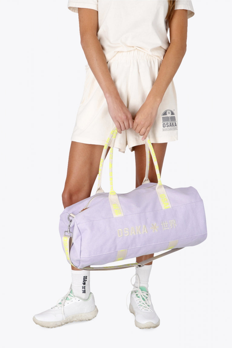 Woman holding the Osaka cotton duffel in light purple with logo. Front view