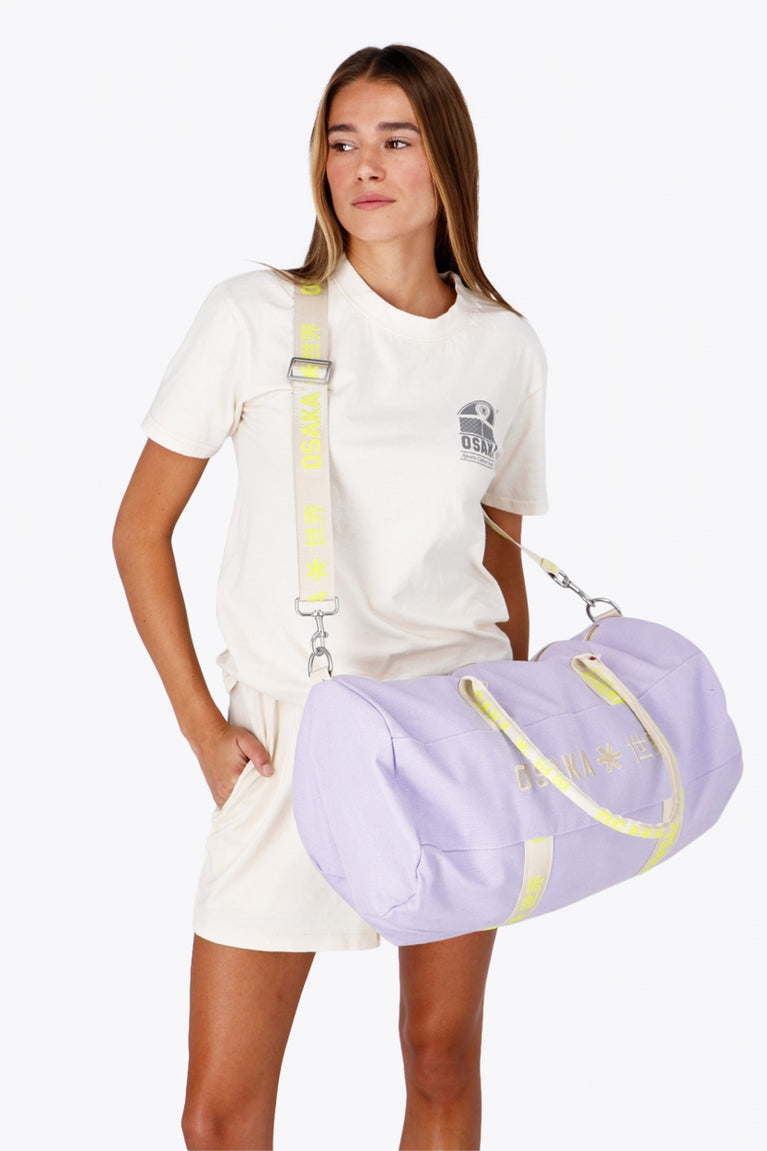 Woman wearing the Osaka cotton duffel in light purple with logo. Front view with strap around