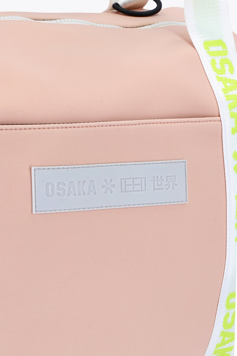 Osaka neoprene duffel bag in powder pink with logo in white on the bag and in green on the straps. Detail logo view