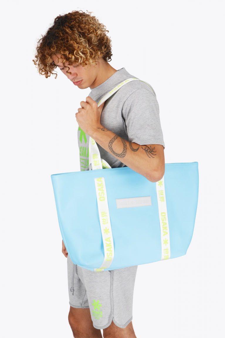 Osaka neoprene Tote bag in light blue with logo in white. Man wearing the bag