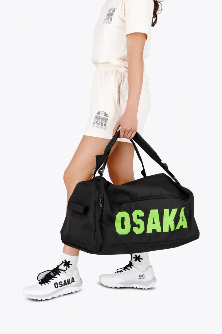 Osaka sports duffel bag in black with logo in green. Woman holding the bag